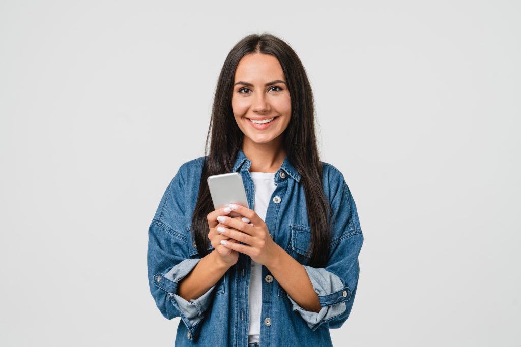 Smiling caucasian young woman girl using smart phone cellphone for e-learning, e-commerce, e-banking online, mobile applications, making bet in casino isolated in white background