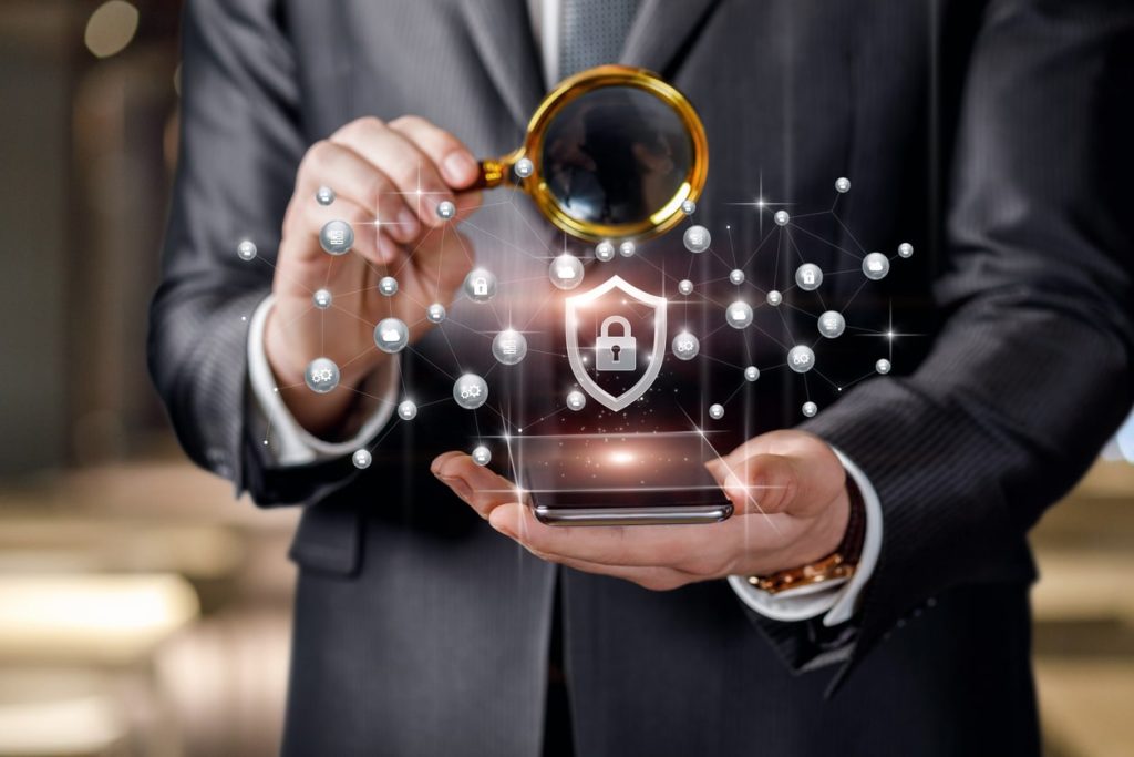 Business man with a magnifying glass watches the protection of the network in a mobile device.
